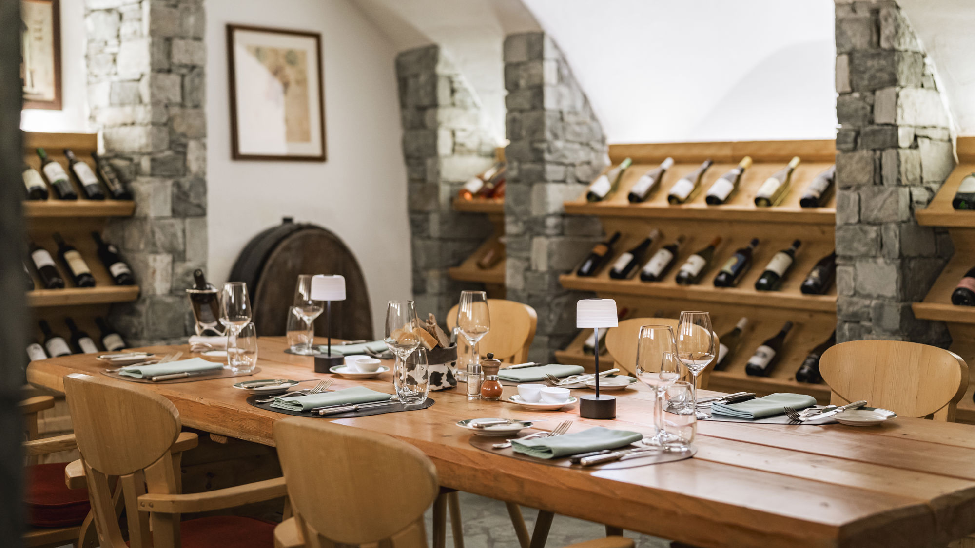 Grande table de dégustation de la Vinothek au Riffelalp Resort 2222m au-dessus de Zermatt, hôtel de luxe 5 étoiles dans les Alpes suisses, entourée de casiers à vins en bois, de voûtes en pierre et d'une sélection de grands crus dans une ambiance chaleureuse et raffinée.