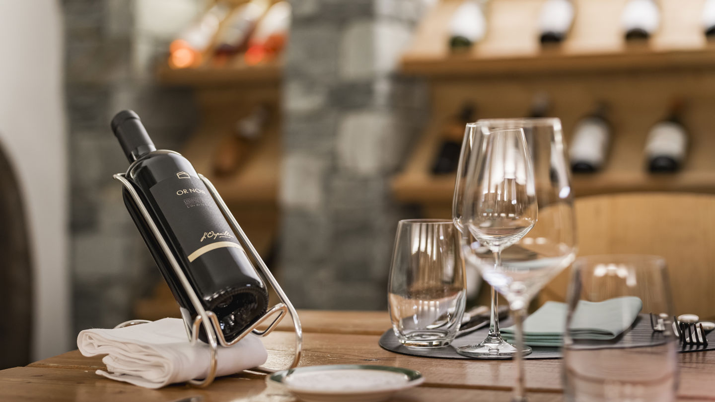 Bouteille de grand cru et verres de dégustation dans la Vinothek du Riffelalp Resort 2222m au-dessus de Zermatt, hôtel de luxe 5 étoiles dans les Alpes suisses, mettant à l'honneur une sélection de vins d'exception dans un cadre raffiné en pierre et en bois.