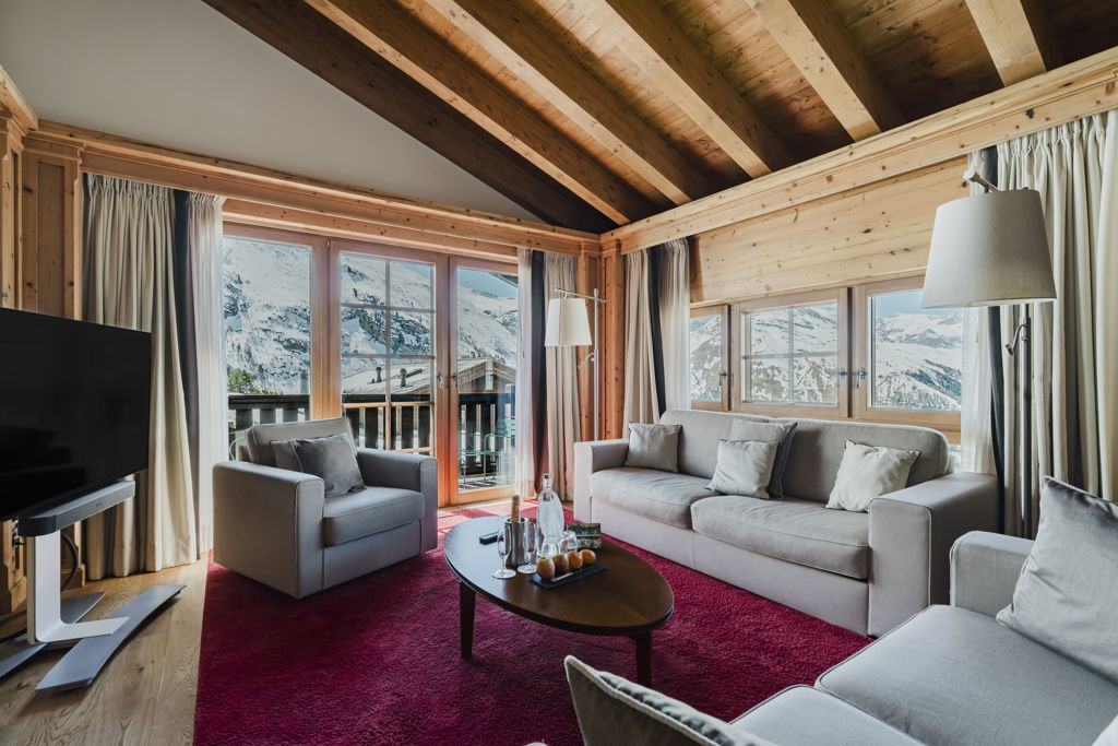 Salon lumineux de la Suite Matterhorn avec canapés, larges fenêtres et panorama sur les Alpes enneigées à Zermatt.