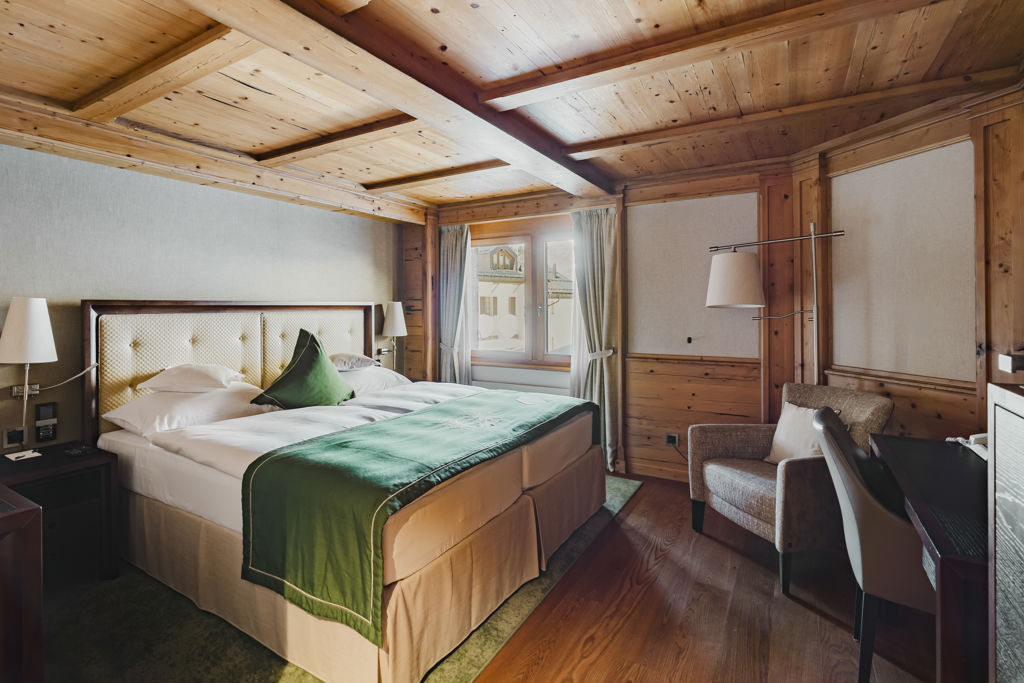 Vue d’ensemble du lit et de l’intérieur chaleureux de la Chambre NATUR Classic en hiver au Riffelalp Resort 2222m à Zermatt, hébergement avec petit-déjeuner et accès au Spa 2222m inclus.