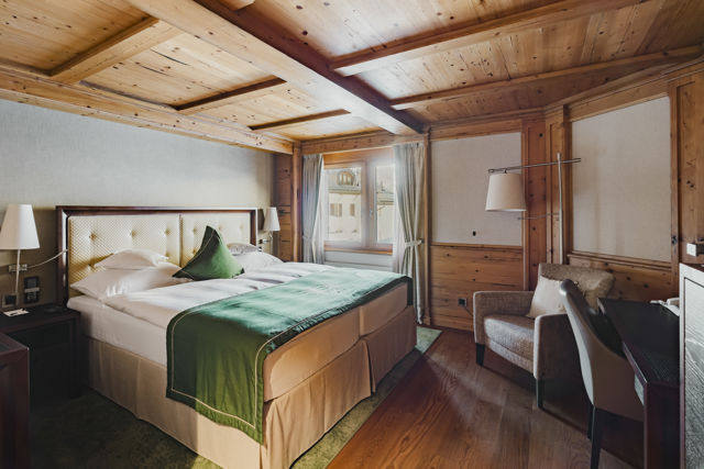 Vue d’ensemble du lit et de l’intérieur chaleureux de la Chambre NATUR Classic en hiver au Riffelalp Resort 2222m à Zermatt, hébergement avec petit-déjeuner et accès au Spa 2222m inclus.