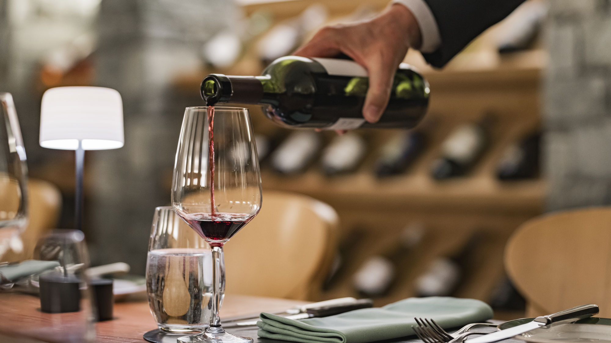 Service du vin dans la Vinothek du Riffelalp Resort 2222m au-dessus de Zermatt, hôtel de luxe 5 étoiles dans les Alpes suisses, où une sélection de grands crus est servie dans un cadre raffiné en pierre et en bois pour une expérience œnologique d'exception.