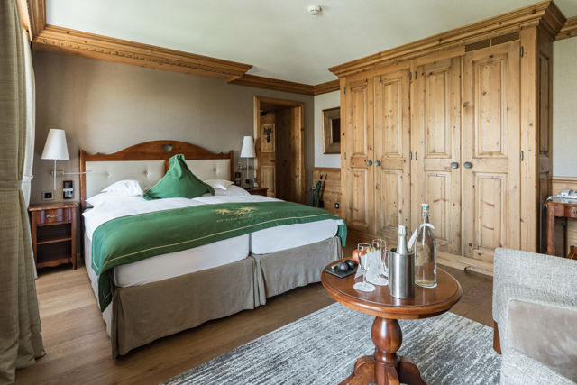 Vue du coin salon vers le lit de la Chambre Matterhorn Classic au Riffelalp Resort 2222m à Zermatt, hébergement spacieux avec décoration alpine élégante.