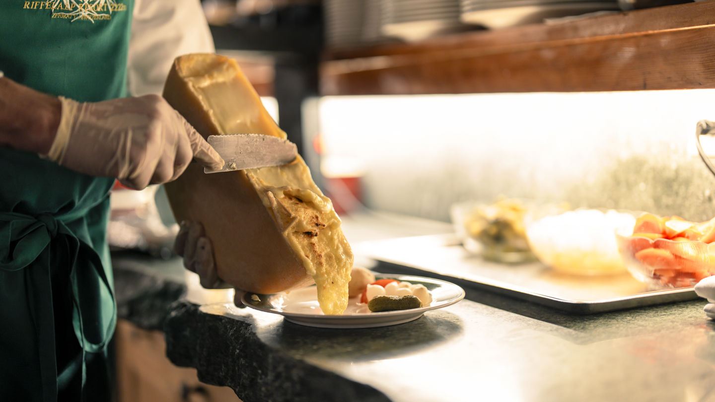 Service traditionnel de raclette au Restaurant Walliserkeller du Riffelalp Resort 2222m à Zermatt, hôtel de luxe 5 étoiles dans les Alpes suisses réputé pour ses spécialités suisses, son fromage fondu et son ambiance de chalet.