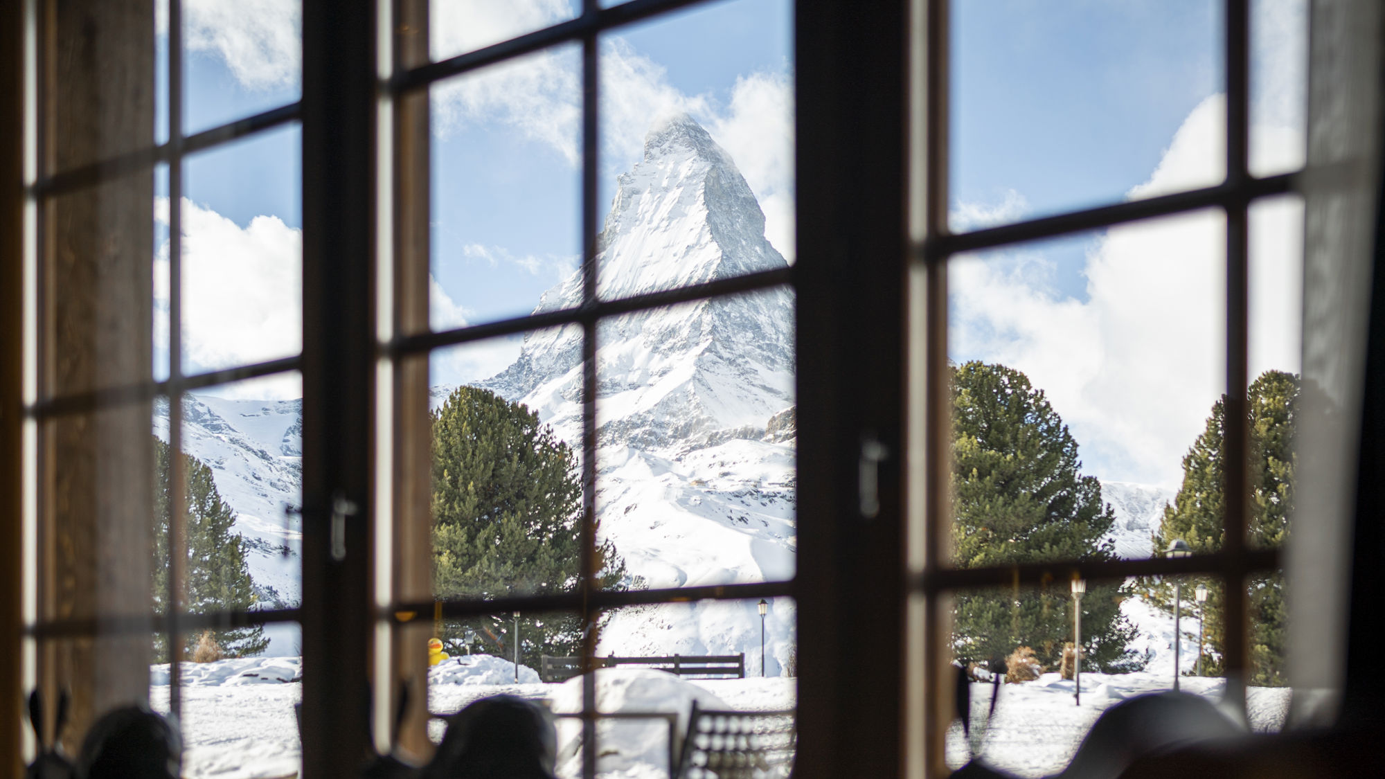 Grandes fenêtres du Bar 2222m encadrant les paysages enneigés du Riffelalp Resort 2222m au-dessus de Zermatt, hôtel de luxe 5 étoiles dans les Alpes suisses offrant une atmosphère lumineuse, un lounge élégant et une vue exceptionnelle sur les Alpes.