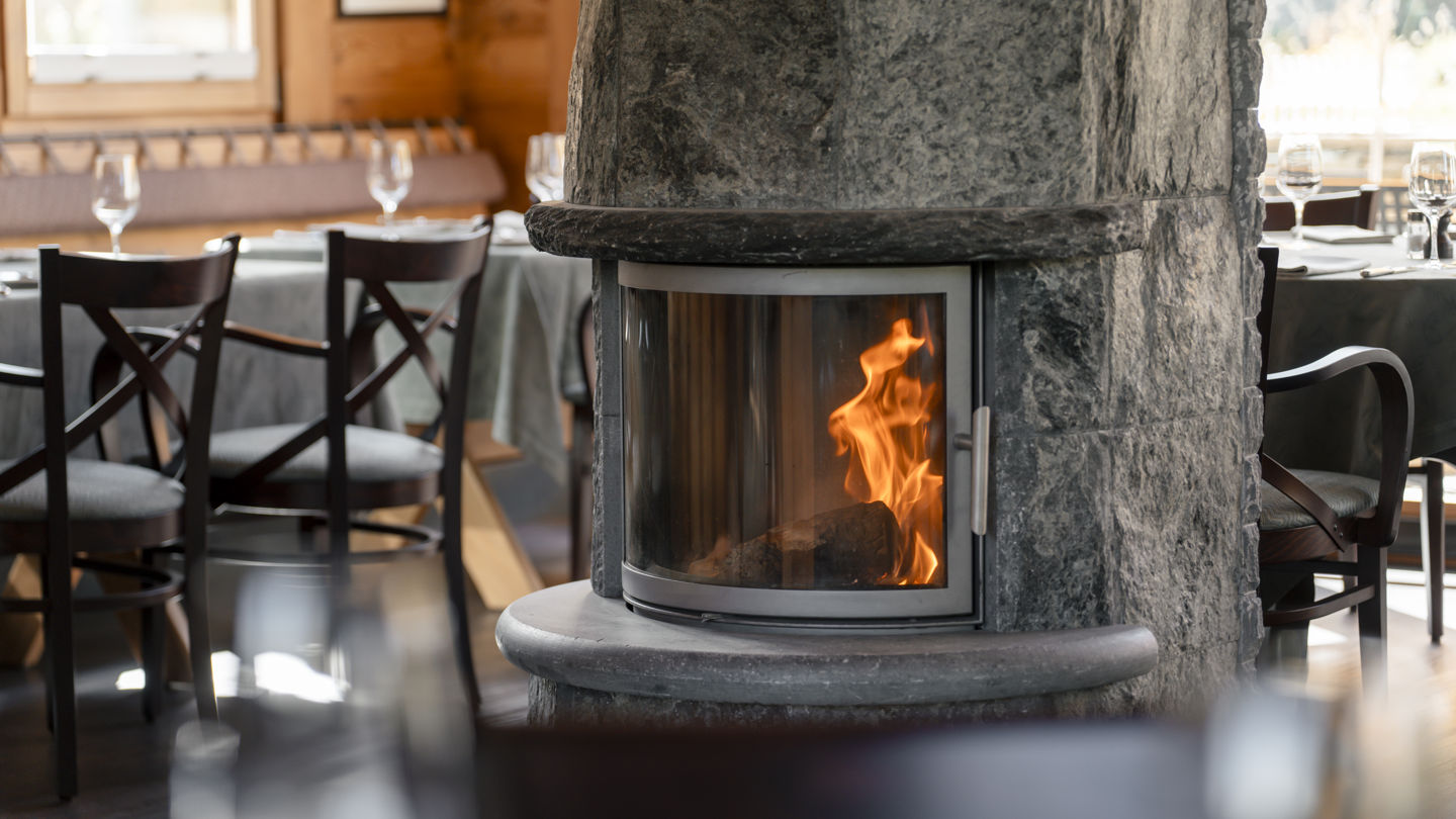 Cheminée centrale et salle du Ristorante Al Bosco au Riffelalp Resort 2222m au-dessus de Zermatt, hôtel de luxe 5 étoiles dans les Alpes suisses, où l'ambiance chaleureuse d'un chalet alpin sublime une cuisine italienne authentique, des pizzas au feu de bois, des pâtes fraîches et des produits locaux de saison.