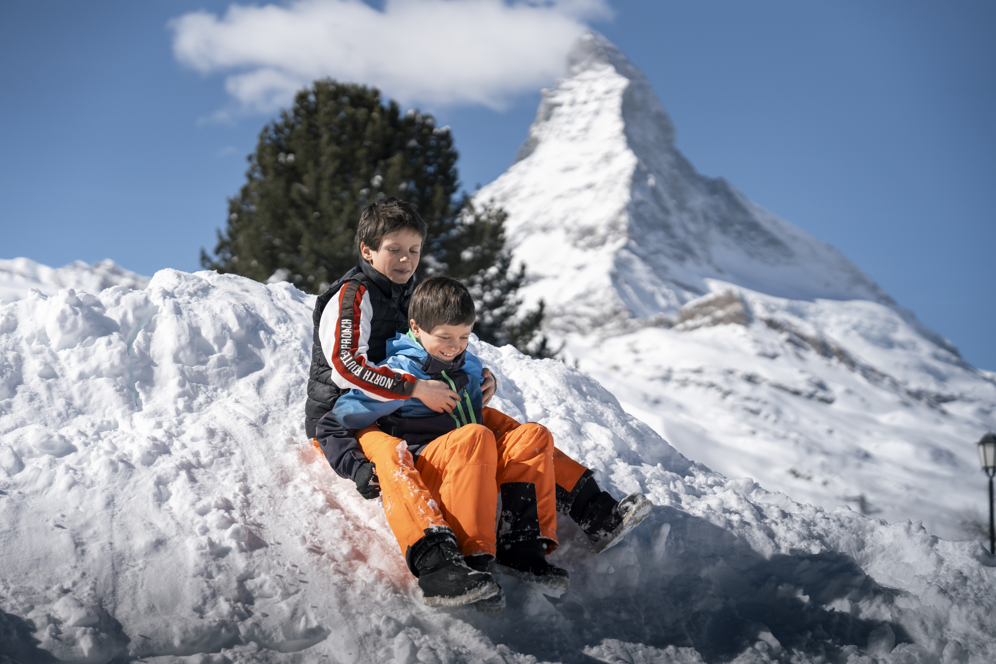 Enfants jouant dans la neige devant le Cervin près du Riffelalp Resort 2222m à Zermatt, hôtel de luxe 5 étoiles dans les Alpes suisses pour des vacances en famille, un séjour nature et des panoramas emblématiques sur le Matterhorn.