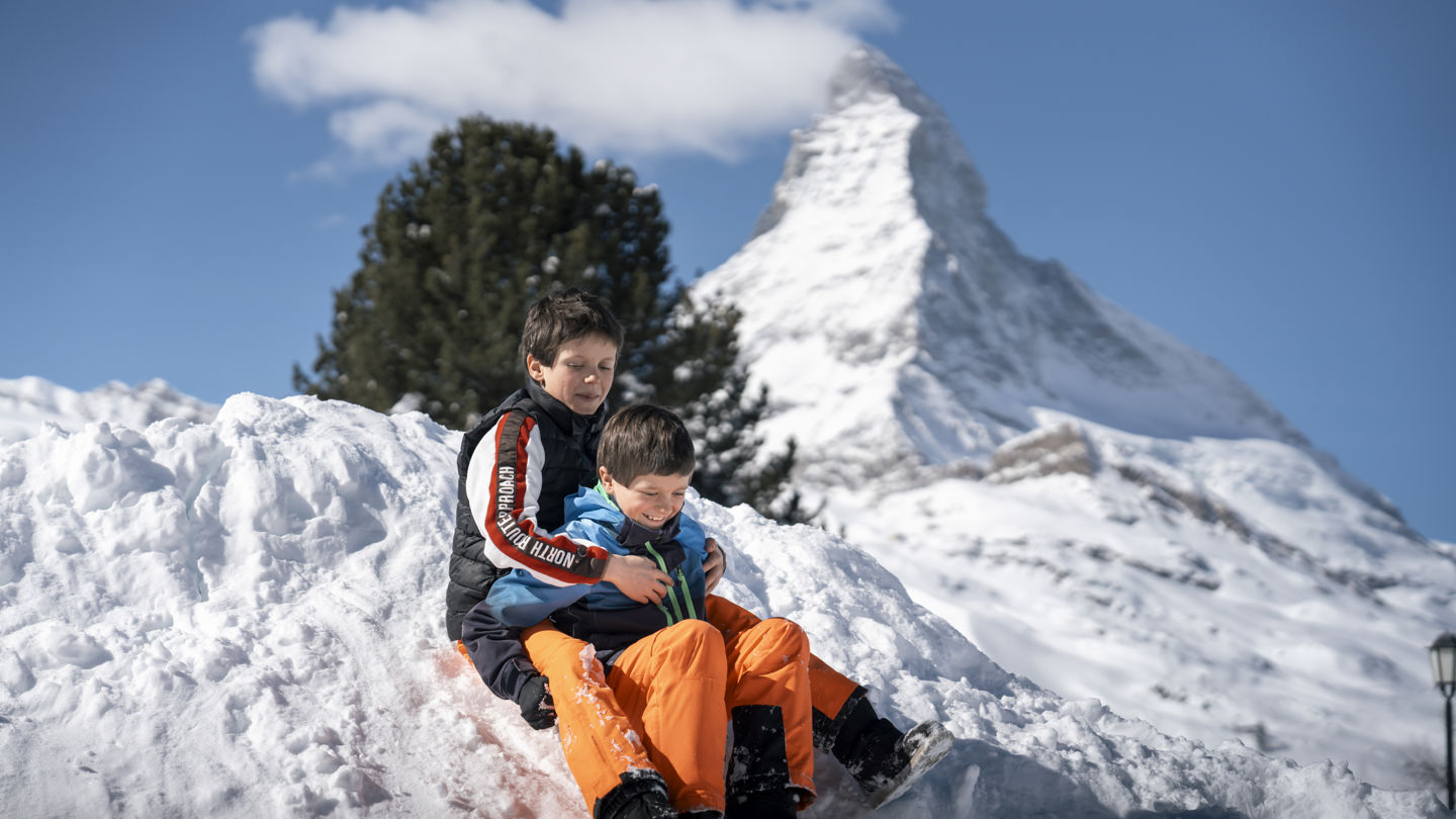 Enfants jouant dans la neige devant le Cervin près du Riffelalp Resort 2222m à Zermatt, hôtel de luxe 5 étoiles dans les Alpes suisses pour des vacances en famille, un séjour nature et des panoramas emblématiques sur le Matterhorn.