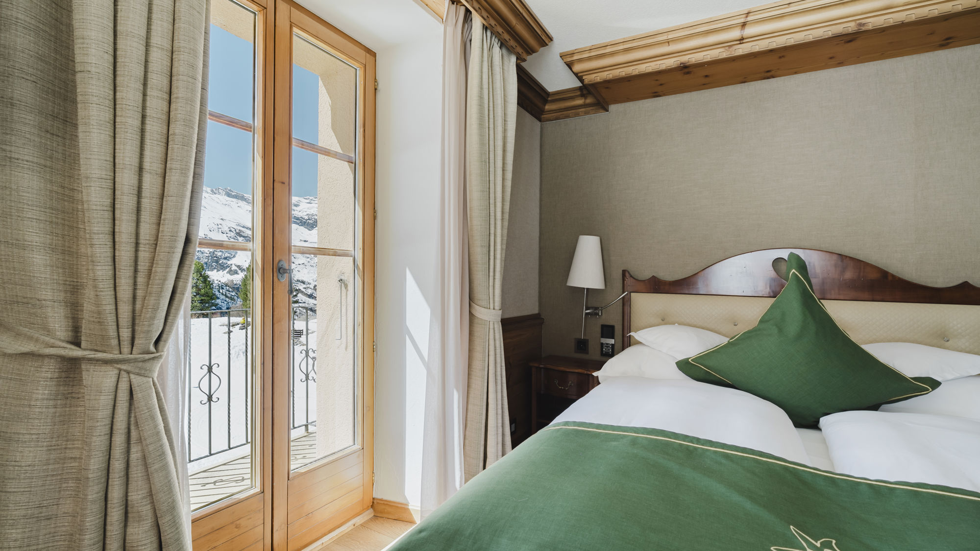 Vue rapprochée du lit et du paysage enneigé depuis la Chambre Matterhorn Classic en hiver au Riffelalp Resort 2222m à Zermatt, hébergement chaleureux avec petit-déjeuner et accès au Spa 2222m inclus.