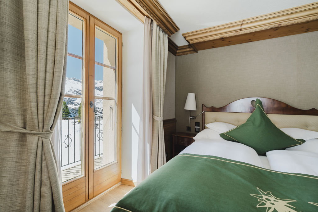 Vue rapprochée du lit et du paysage enneigé depuis la Chambre Matterhorn Classic en hiver au Riffelalp Resort 2222m à Zermatt, hébergement chaleureux avec petit-déjeuner et accès au Spa 2222m inclus.
