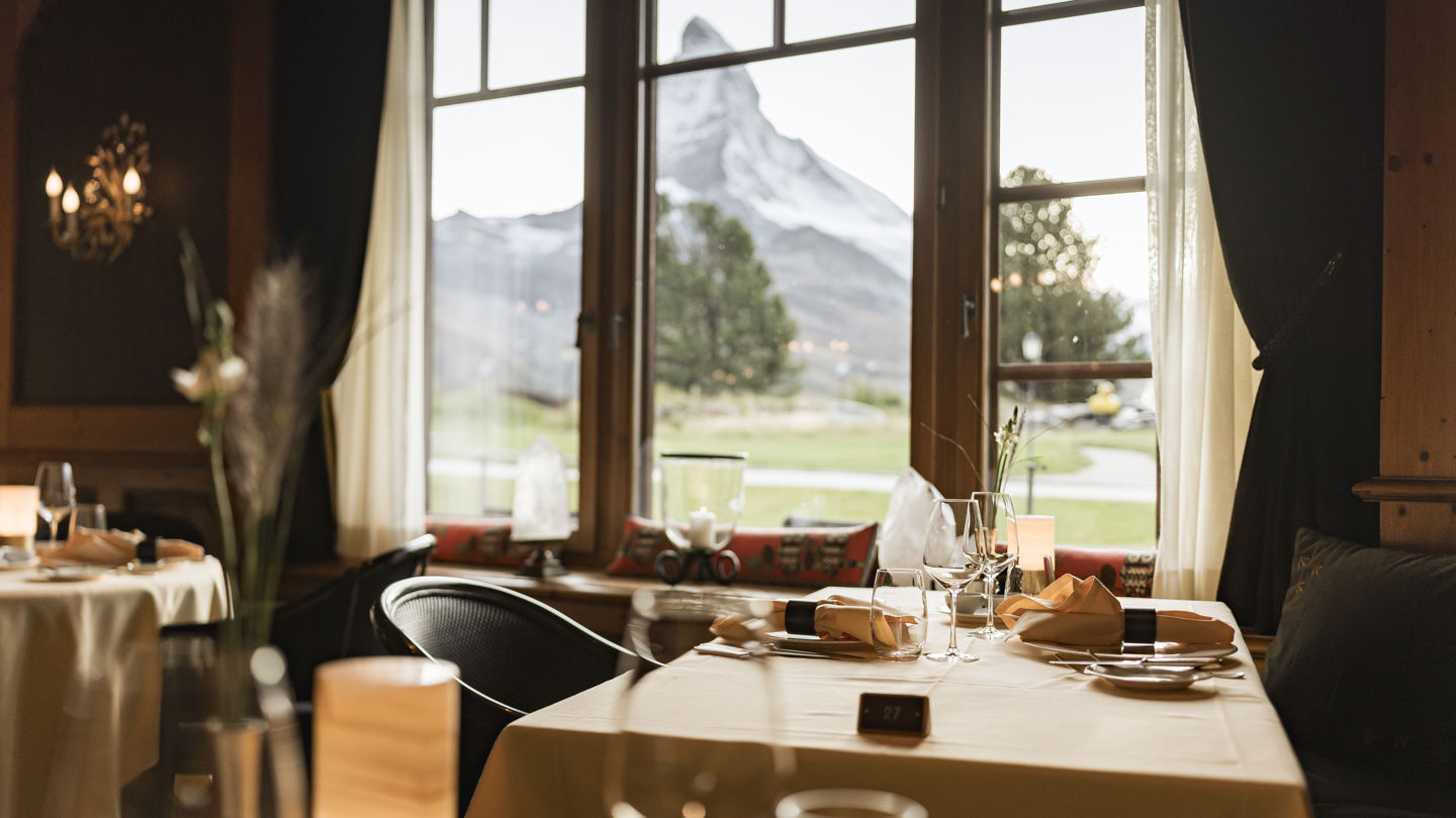 Salle lumineuse du Restaurant Alexandre en été au Riffelalp Resort 2222m à Zermatt, hôtel de luxe 5 étoiles dans les Alpes suisses, avec tables dressées, boiseries élégantes et atmosphère romantique pour un dîner gastronomique.