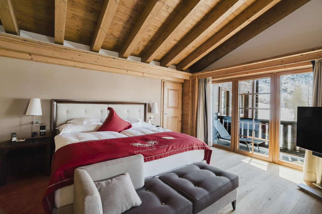 Chambre lumineuse de la Suite Matterhorn avec lit double et accès au balcon donnant sur les montagnes enneigées à Zermatt.