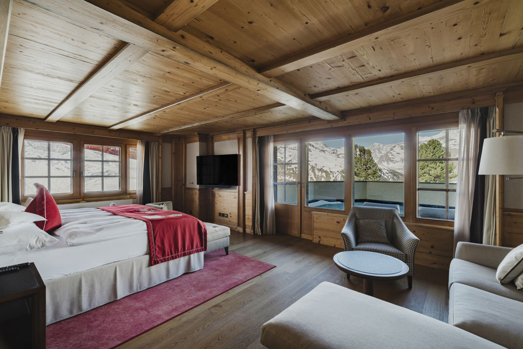 Vue d’ensemble de la Matterhorn Deluxe Junior Suite au Riffelalp Resort 2222m à Zermatt, avec lit double, coin salon, intérieur alpin en bois et accès à la terrasse.