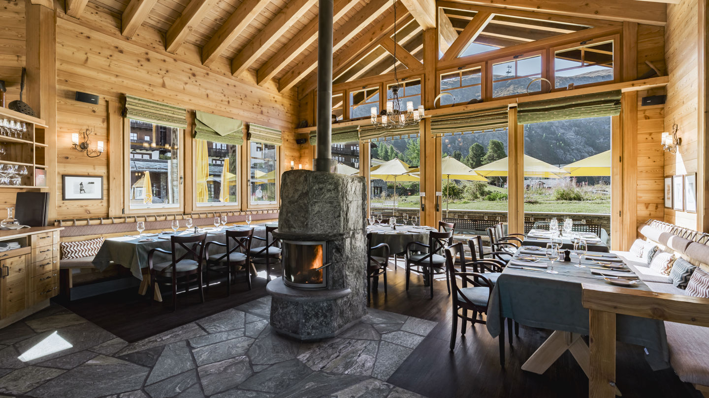 Salle lumineuse du Ristorante Al Bosco au Riffelalp Resort 2222m au-dessus de Zermatt, hôtel de luxe 5 étoiles dans les Alpes suisses, avec boiseries, grandes baies vitrées et ambiance de chalet pour un repas italien en montagne.