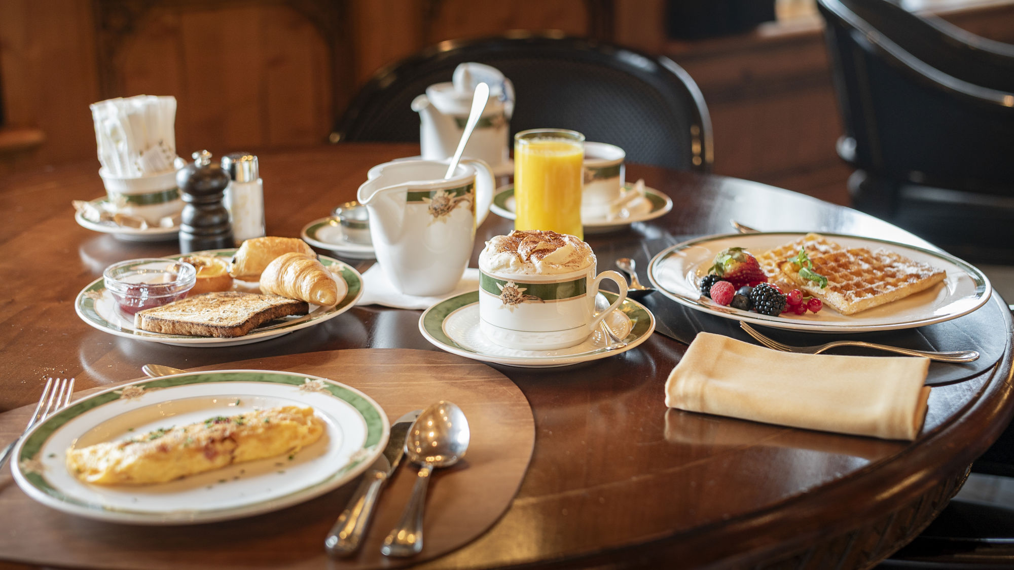 Petit-déjeuner complet servi au Riffelalp Resort 2222m au-dessus de Zermatt, hôtel de luxe 5 étoiles dans les Alpes suisses, avec omelette, viennoiseries, gaufre, fruits frais, café et jus de fruits dans une ambiance chaleureuse et raffinée.