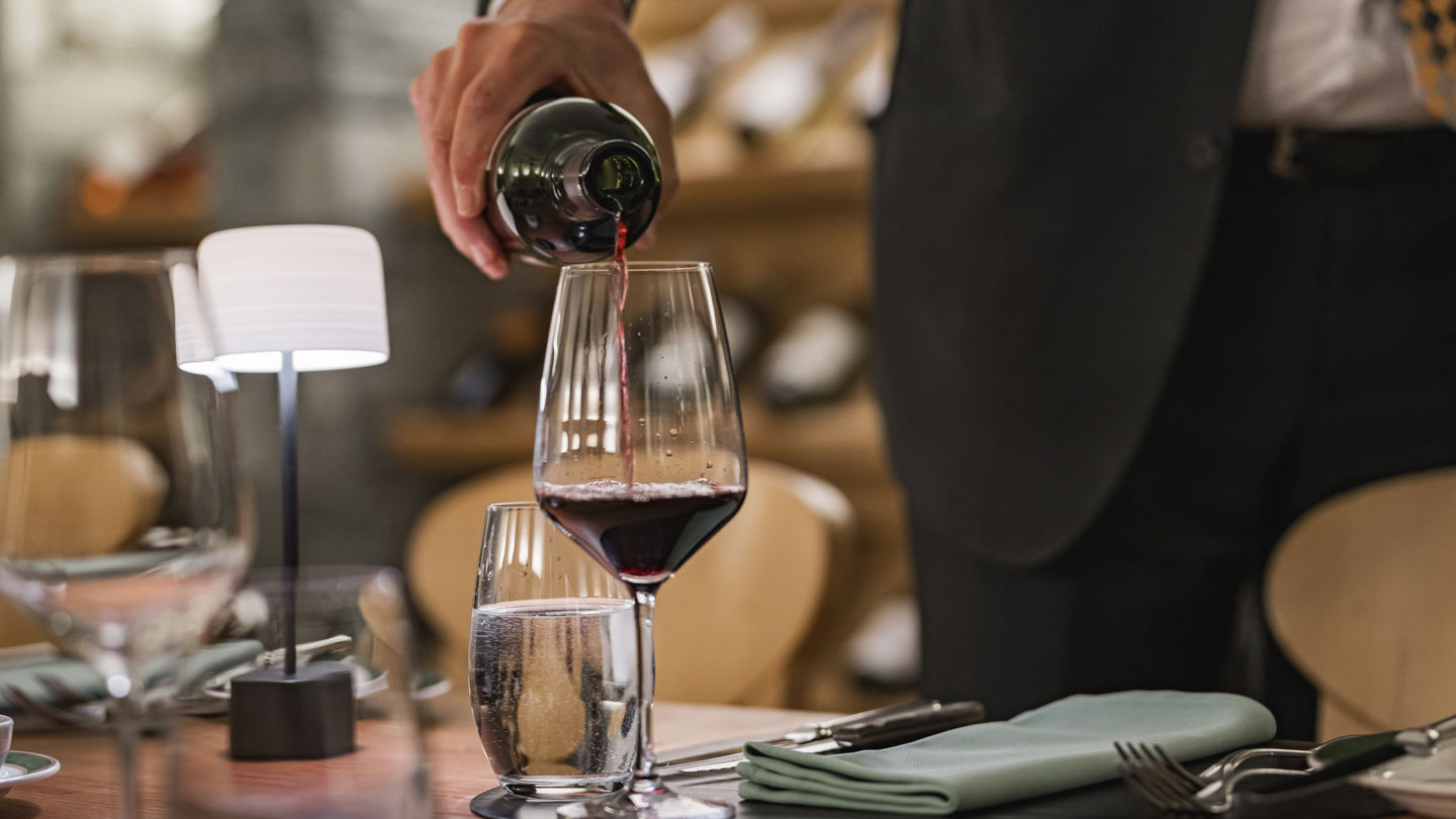 Sommelier servant un verre de vin dans la Vinothek du Riffelalp Resort 2222m au-dessus de Zermatt, hôtel de luxe 5 étoiles dans les Alpes suisses, offrant une dégustation de grands crus dans une atmosphère élégante et authentique.