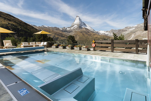 Terrasse de la piscine extérieure du Spa 2222m au Riffelalp Resort 2222m à Zermatt, espace de détente avec transats et vue sur les montagnes des Alpes suisses.