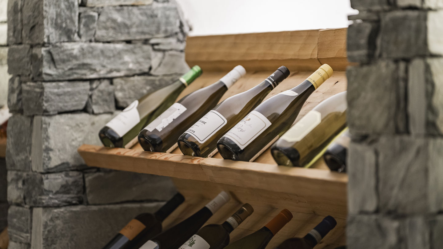 Sélection de bouteilles exposées dans la Vinothek du Riffelalp Resort 2222m au-dessus de Zermatt, hôtel de luxe 5 étoiles dans les Alpes suisses, où les grands crus sont présentés sur des casiers en bois dans un cadre authentique de pierre naturelle.