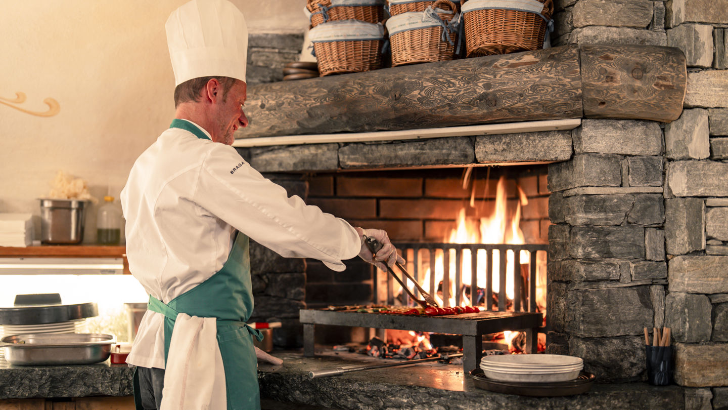 Chef préparant des grillades devant le feu de bois au Restaurant Walliserkeller du Riffelalp Resort 2222m au-dessus de Zermatt, hôtel de luxe 5 étoiles dans les Alpes suisses mettant en valeur les viandes de qualité et les spécialités régionales.