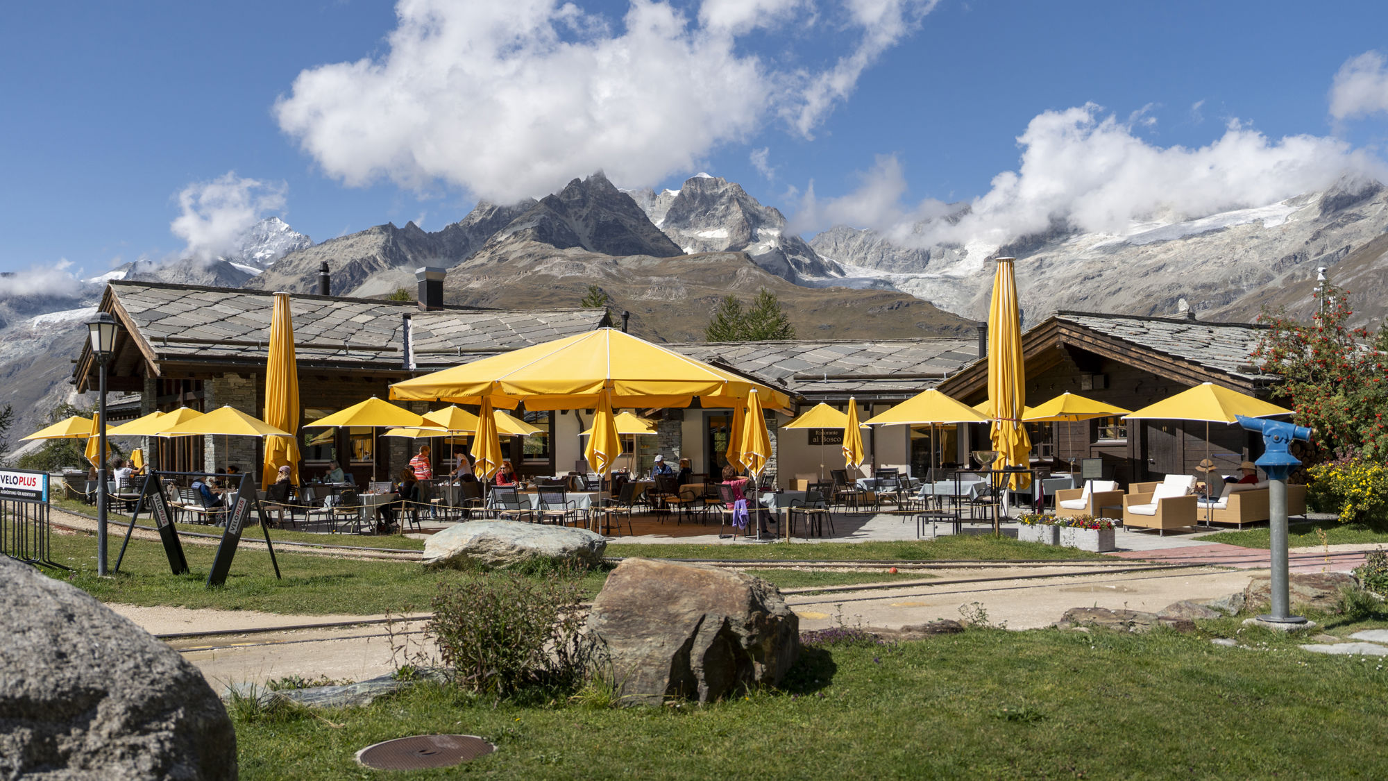 Vue extérieure estivale du Ristorante Al Bosco au Riffelalp Resort 2222m au-dessus de Zermatt, hôtel de luxe 5 étoiles dans les Alpes suisses, offrant une cuisine italienne raffinée, des spécialités préparées avec des ingrédients alpins suisses et une vue exceptionnelle sur le Cervin.