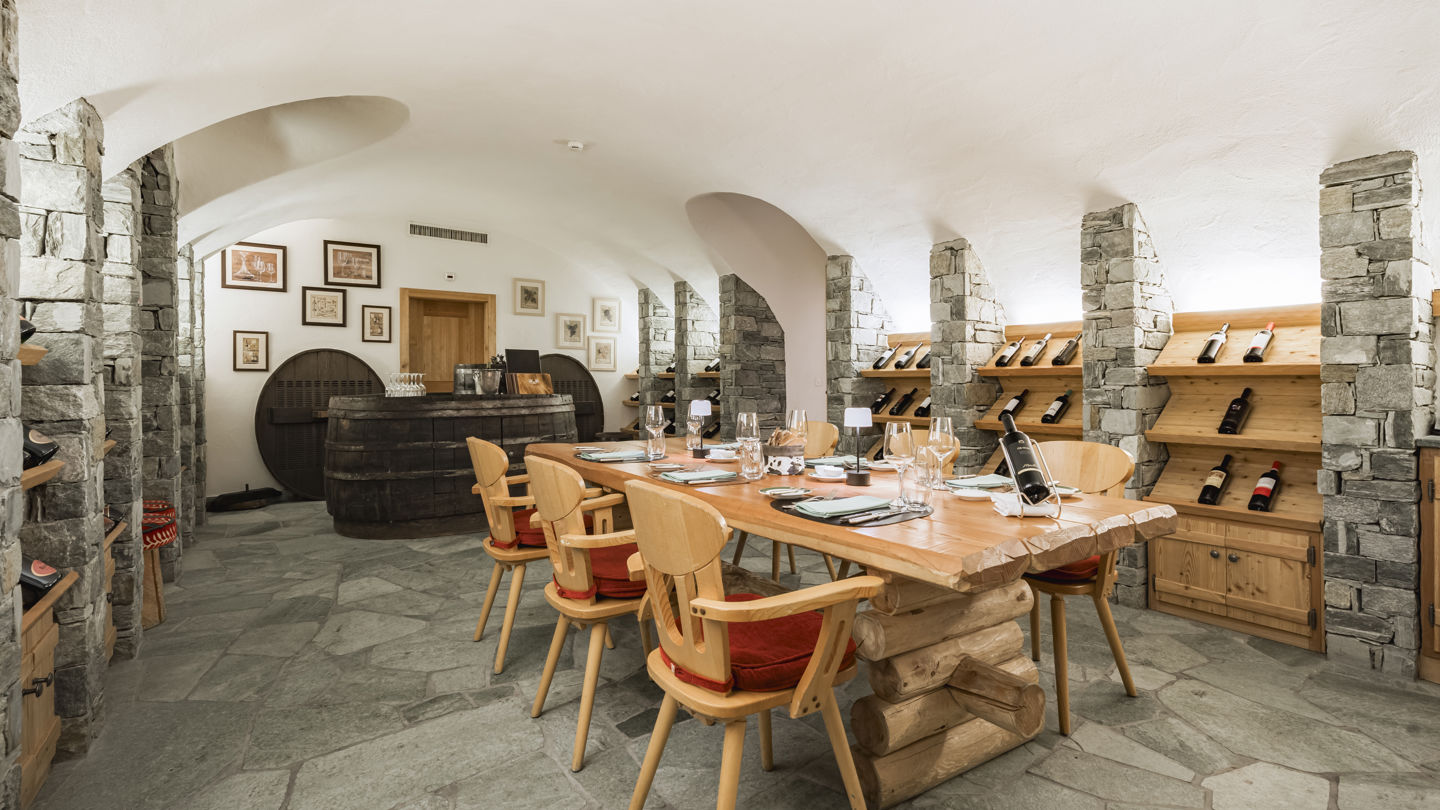 Salle de dégustation de la Vinothek au Riffelalp Resort 2222m au-dessus de Zermatt, hôtel de luxe 5 étoiles dans les Alpes suisses, où les voûtes en pierre, les présentoirs à vins en bois et les grandes tables créent un cadre élégant pour une expérience œnologique raffinée.