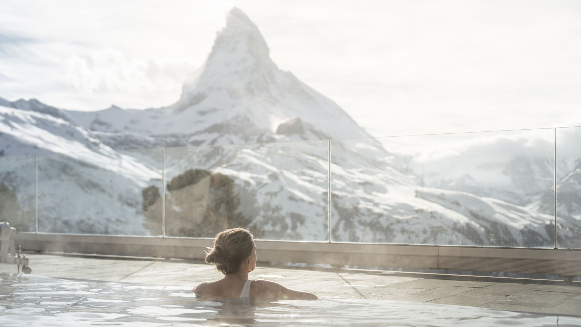Client profitant de la piscine extérieure en hiver du Spa 2222m au Riffelalp Resort 2222m à Zermatt avec le Cervin en toile de fond, expérience bien-être unique dans les Alpes suisses.