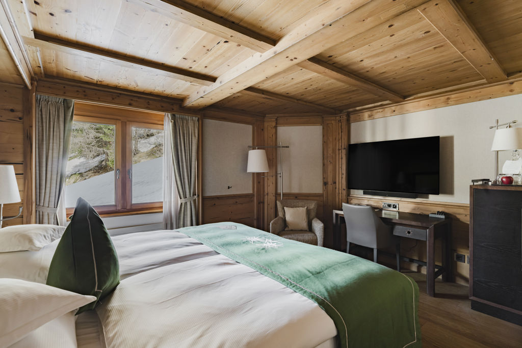 Vue du lit, du bureau et du coin détente de la Chambre NATUR Classic en hiver au Riffelalp Resort 2222m à Zermatt, hébergement chaleureux avec petit-déjeuner et accès au Spa 2222m inclus.